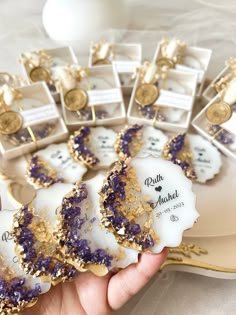 purple and gold decorated cookies are displayed on a platter with white boxes in the background