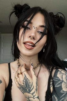 a woman with black hair and tattoos on her chest posing for the camera, holding her hands to her face