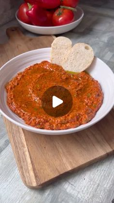 a white bowl filled with sauce and chips on top of a wooden cutting board next to tomatoes