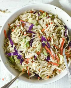 a white bowl filled with coleslaw and carrots next to a silver spoon