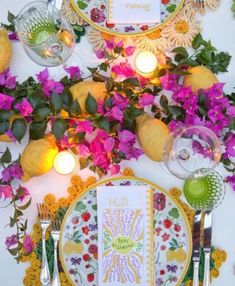 a table topped with plates and flowers next to candles on top of a white wall