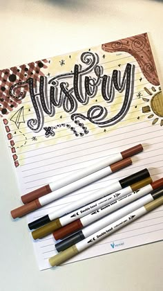 some pens are sitting on top of a piece of paper with the word history written in cursive writing