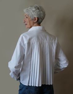 an older woman wearing a white blouse and jeans looking off to the side with her hands on her hips