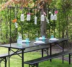 a picnic table set up outside with flowers hanging from the branches and plates on it