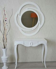 a white table with a mirror on it next to a flower vase and a plant