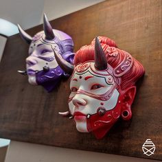 two masks are hanging on the wall next to each other, with horns sticking out of them