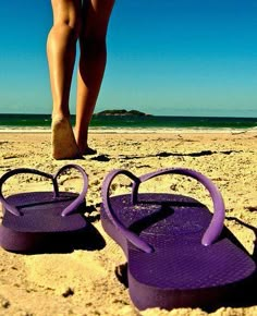 pair of purple flip flops on sandy beach with blue sky and ocean in background