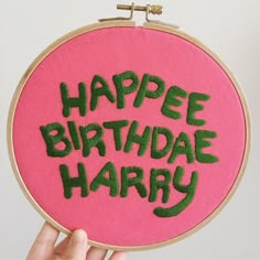 a hand holding up a pink and green embroidered birthday sign with the words happy birthday harry on it