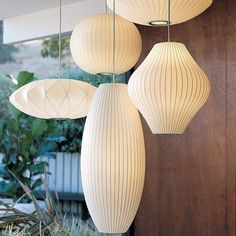 three white lamps hanging from the ceiling in front of a building with plants and bushes