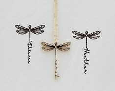 three dragonflys hanging from a chain on a white background with the word love spelled in cursive writing