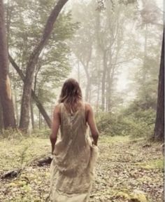 a woman walking in the woods with her back turned to the camera, wearing a long dress