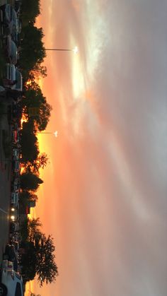 the sun is setting behind some trees and cars parked on the side of the road