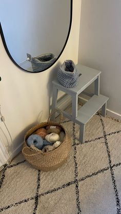 there is a basket with rocks in it on the floor next to a wall mirror