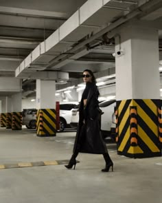 a woman in black coat and sunglasses walking through parking garage