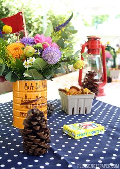 a pine cone vase filled with flowers on top of a blue table cloth next to other items