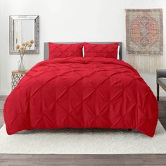 a bed with red comforter and pillows in a room next to a rug on the floor