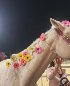 a woman is petting a white horse with flowers on it's head at night