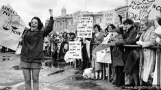 a woman is walking down the street with her arms in the air as people hold up signs