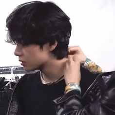 a man with black hair wearing a leather jacket and holding his hand to his ear