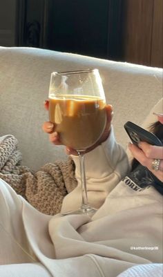 a woman sitting on a couch holding a glass of wine and cell phone in her hand