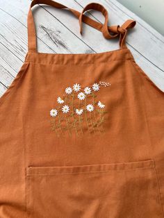 an orange apron with daisies embroidered on the front and back, sitting on a wooden table