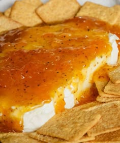 a plate full of tortilla chips with cheese and sauce on top, next to crackers