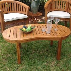 two wooden chairs sitting next to each other on top of a grass covered field with a bowl of fruit