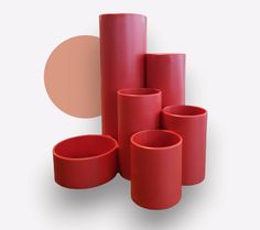 several red vases are stacked up on top of each other in front of a beige circle