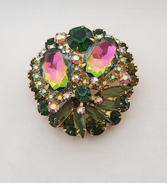 Stunning Juliana also known by name DeLizza & Elster Brooch in very good pre-loved condition.  Measures 1 3/4" in diameter. Brooch is featuring  two larger watermelon rhinestones (they mix of green and pink colors)  dark green,  olivine, pink  and Aurora Bareilles rhinestones. Brooch is identified for being Juliana by construction and setting of the stones. The original was sold with paper hang tag was used on jewelry and most likely was discarded by original owner.  Juliana jewelry was named after Frank DeLizza mother.  This style was always carried by DeLizza & Elster. Highly collectable.  Perfect for any occasion. Juliana Jewelry, Green And Pink, Rhinestone Brooches, Hang Tags, Antique Jewelry, Halloween Shopping, Pink Color, Bead Work, Vintage Antiques