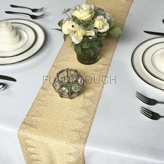 the table is set with silverware and white flowers in a glass vase on it