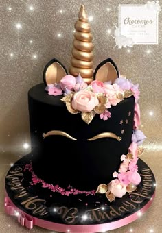 a black cake decorated with pink flowers and a gold unicorn's horn on top