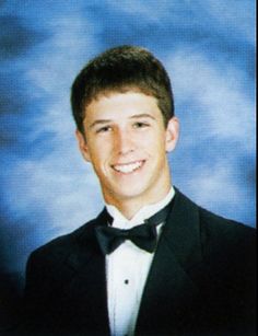 a young man in a tuxedo and bow tie smiling at the camera with a blue background