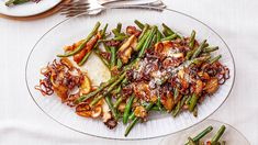 a white plate topped with green beans and onions next to another plate filled with food