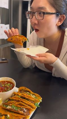 a woman eating food from a plate on top of a table next to a bowl of soup