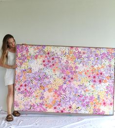 a woman is holding up a large painting