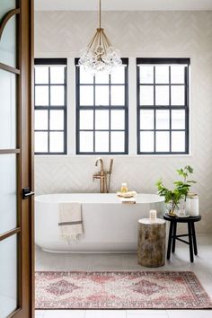 a white bath tub sitting next to a window in a bathroom under a chandelier