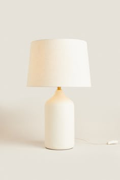 a white table lamp with a beige shade on the base and a cord plugged in