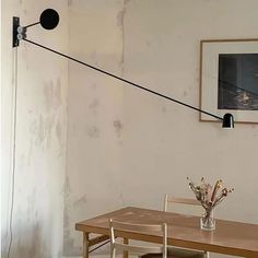 a wooden table with two chairs and a vase on it next to a wall mounted light