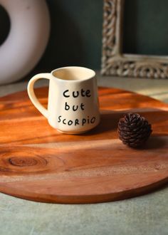 a white coffee cup sitting on top of a wooden tray next to a pine cone