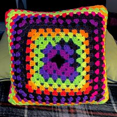 a colorful crocheted square pillow sitting on top of a bed