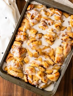 a pan filled with cinnamon rolls covered in icing on top of a wooden table