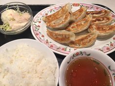 two plates with food on them sitting on a table next to bowls of rice and sauce