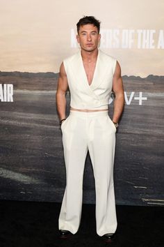 a man standing in front of a wall wearing white pants and a suit with his hands on his hips