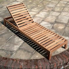 a wooden chaise lounge sitting on top of a brick patio next to a stone wall