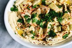 a white bowl filled with hummus, artichokes and parsley on top