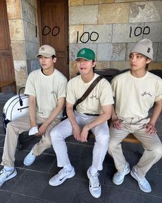 three young men sitting on a bench in front of a building with numbers written on it