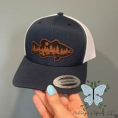 Join the retro trucker hat trend with our Bass Fish Mountain Leather Patch Adult Unisex Cap! Made with high-quality materials, this cap features a leather patch showcasing a bass fish and mountains. Perfect for outdoor enthusiasts, this hat adds a stylish touch to any outfit while protecting you from the sun. The leather patch designs are affixed with adhesive for very secure attachment to the hat. Due to monitor colors, patches and hat colors may be slightly different in person. Custom leather patch hats are made from laser-engraved LEATHERETTE material.  Availiable in YP Classics and Richardson 112! Rhinestone Hoodie, Patch Hats, Bass Fish, Embroidered Initials, Nurse Hat, Hat Patches, Leather Hats, Thanksgiving Outfit, Patch Design