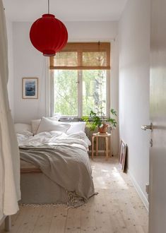 a bedroom with white walls and wood flooring has a red lantern hanging over the bed