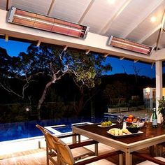 an outdoor dining area is lit up at night with lights on the ceiling and large windows