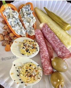 an assortment of meats and vegetables on a paper plate with pickles, olives